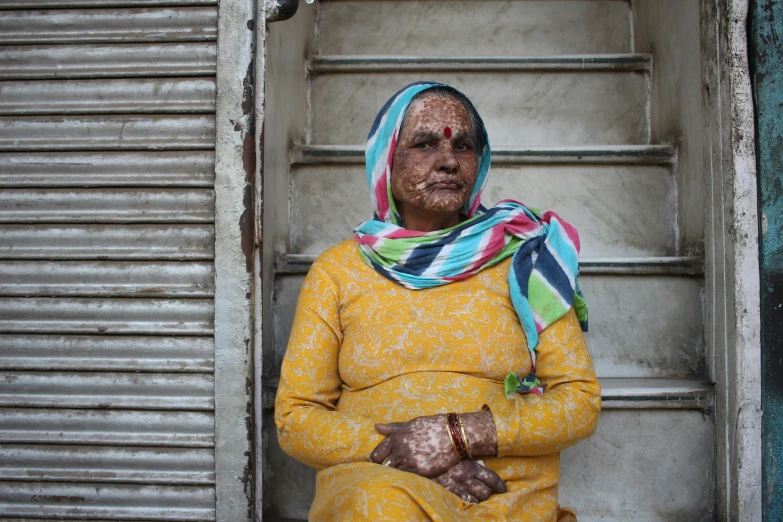 an old woman in yellow outfit and scarf sitting on a staircase