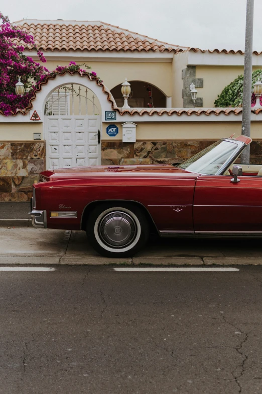 an old red convertible car parked next to a stone wall