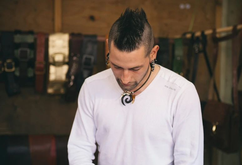 man in white shirt looking down with metal objects on wall in background