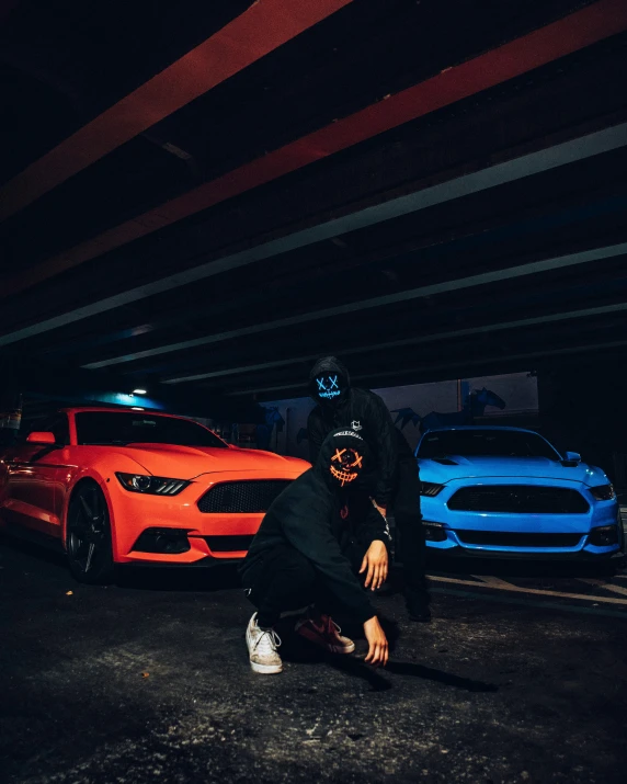 man in a black outfit kneeling down in front of some colorful cars