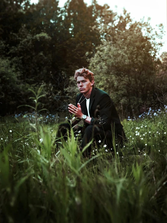 a man in a suit sits in a field holding a microphone