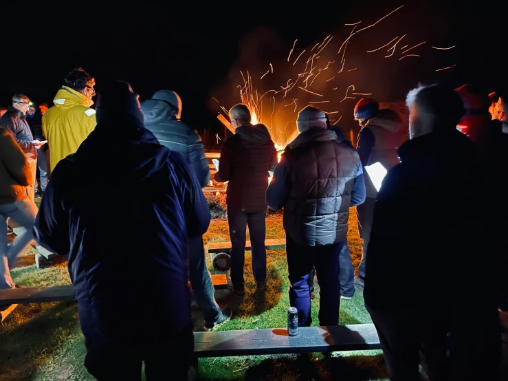 a group of people standing around a fire pit at night