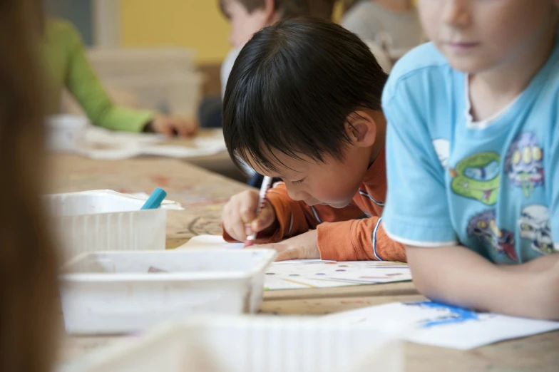 small boy in blue shirt writing on a notebook with a pencil