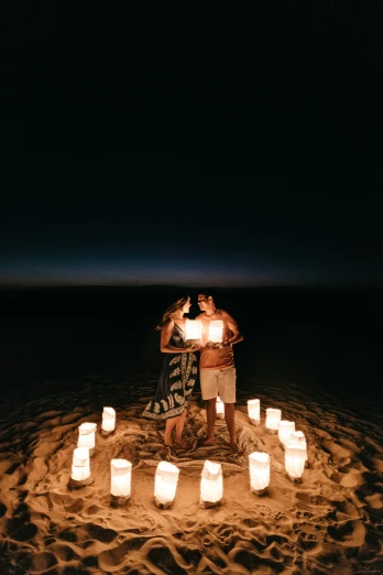 a couple standing on top of a sandy beach next to a lot of candles