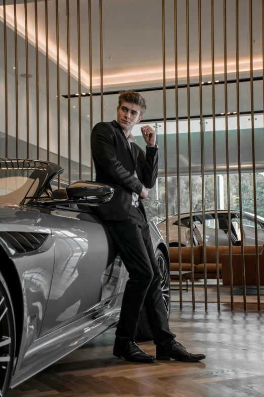 a young man dressed in black leans against a sports car