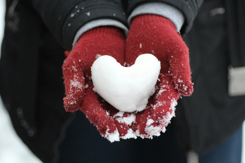 a hand in the snow holding a heart shape piece