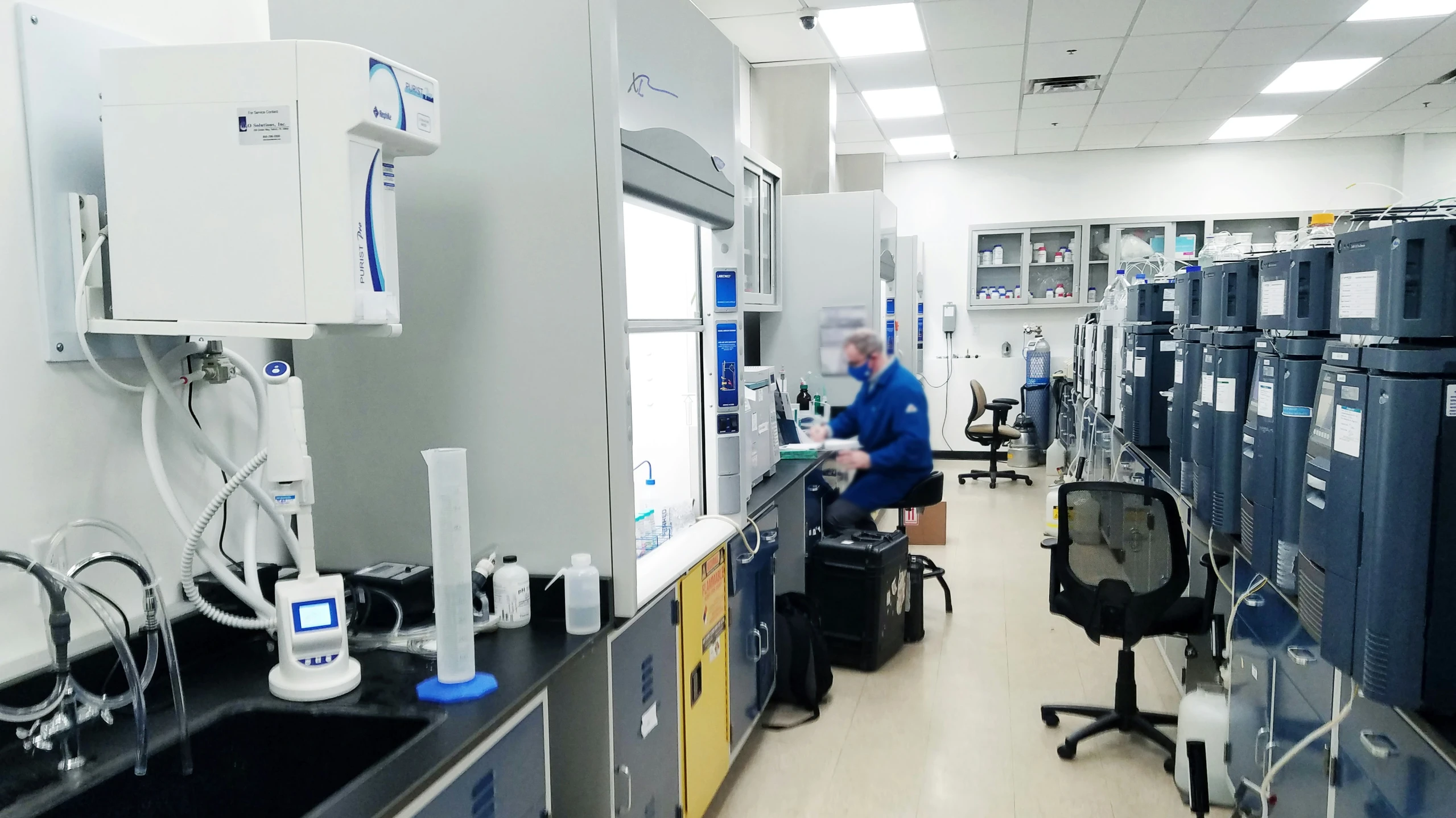 a man in a blue lab coat is standing by several industrial machines