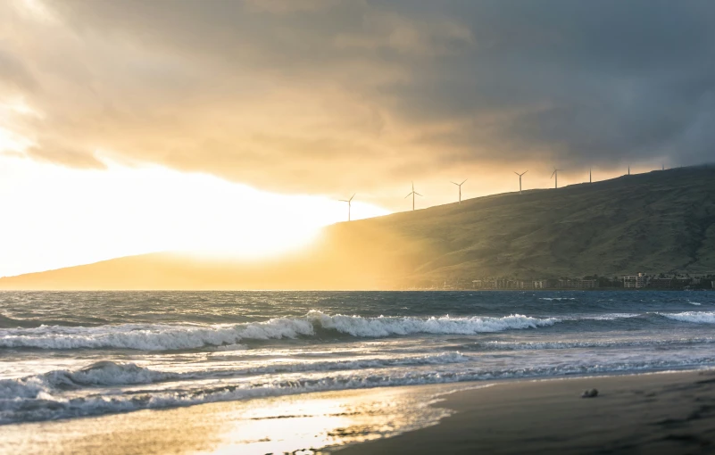 some wind mills are near the water and a hill