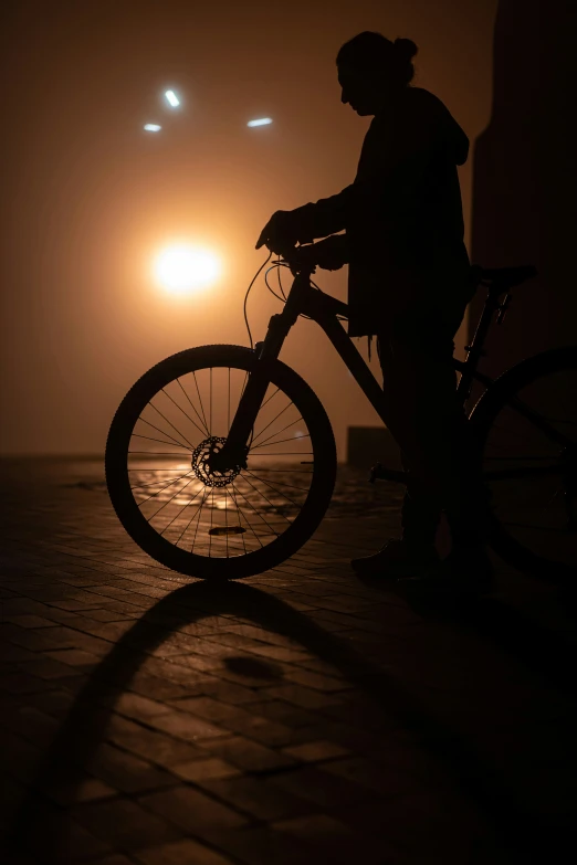 a man stands on his bike while the sun sets