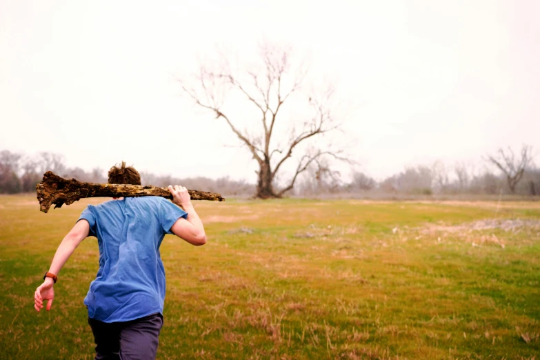 a man carrying an old, worn tree log across a field