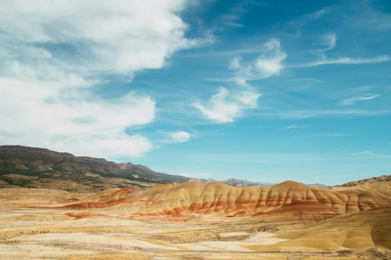 some hills and dirt with white clouds in the sky