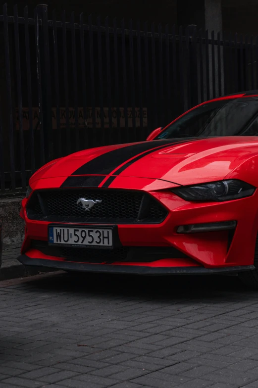 a red mustang car with black stripes sits parked in the street