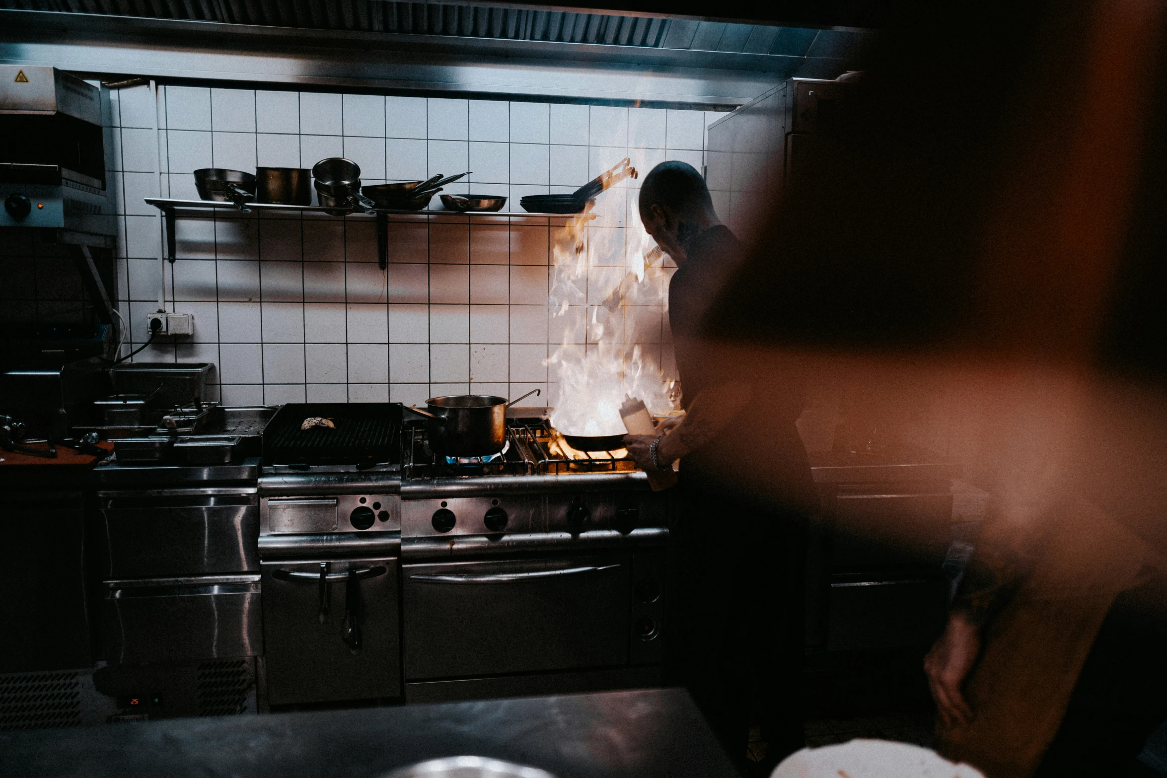 man cooking food in kitchen with flames in the air