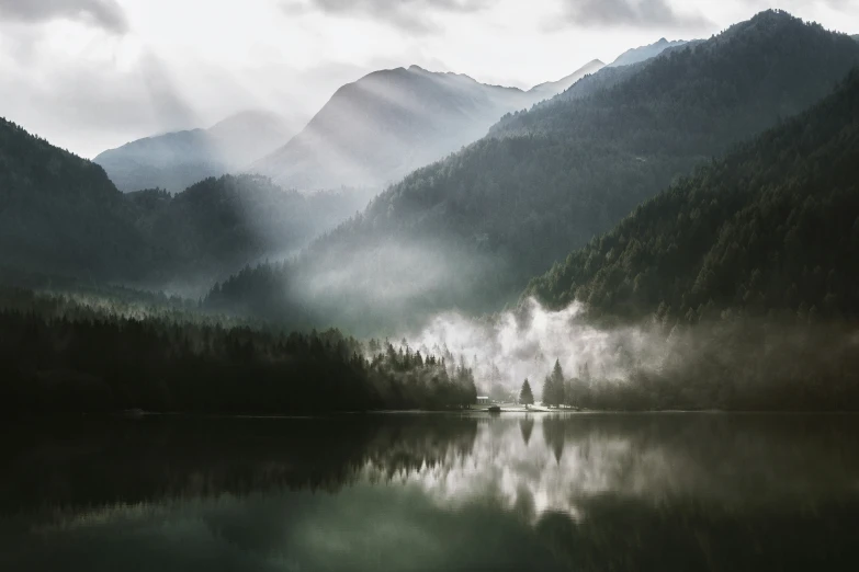 a misty and foggy mountain lake with trees reflected on the water