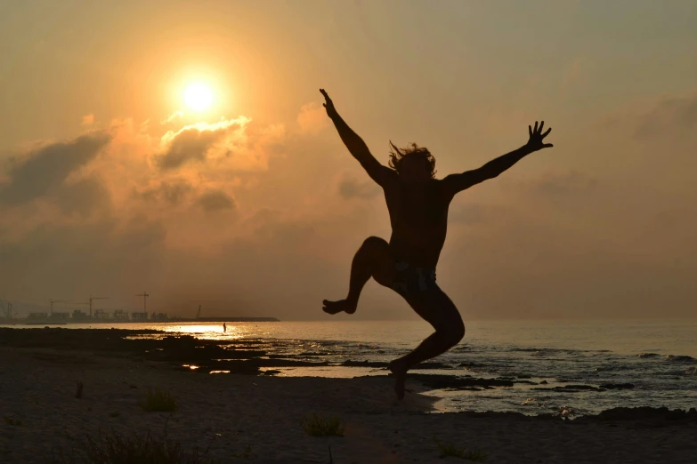 silhouette of man jumping from shore in front of sunset