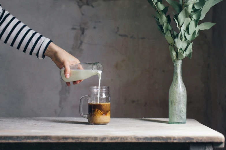 a person pours sugar into a pitcher next to a vase