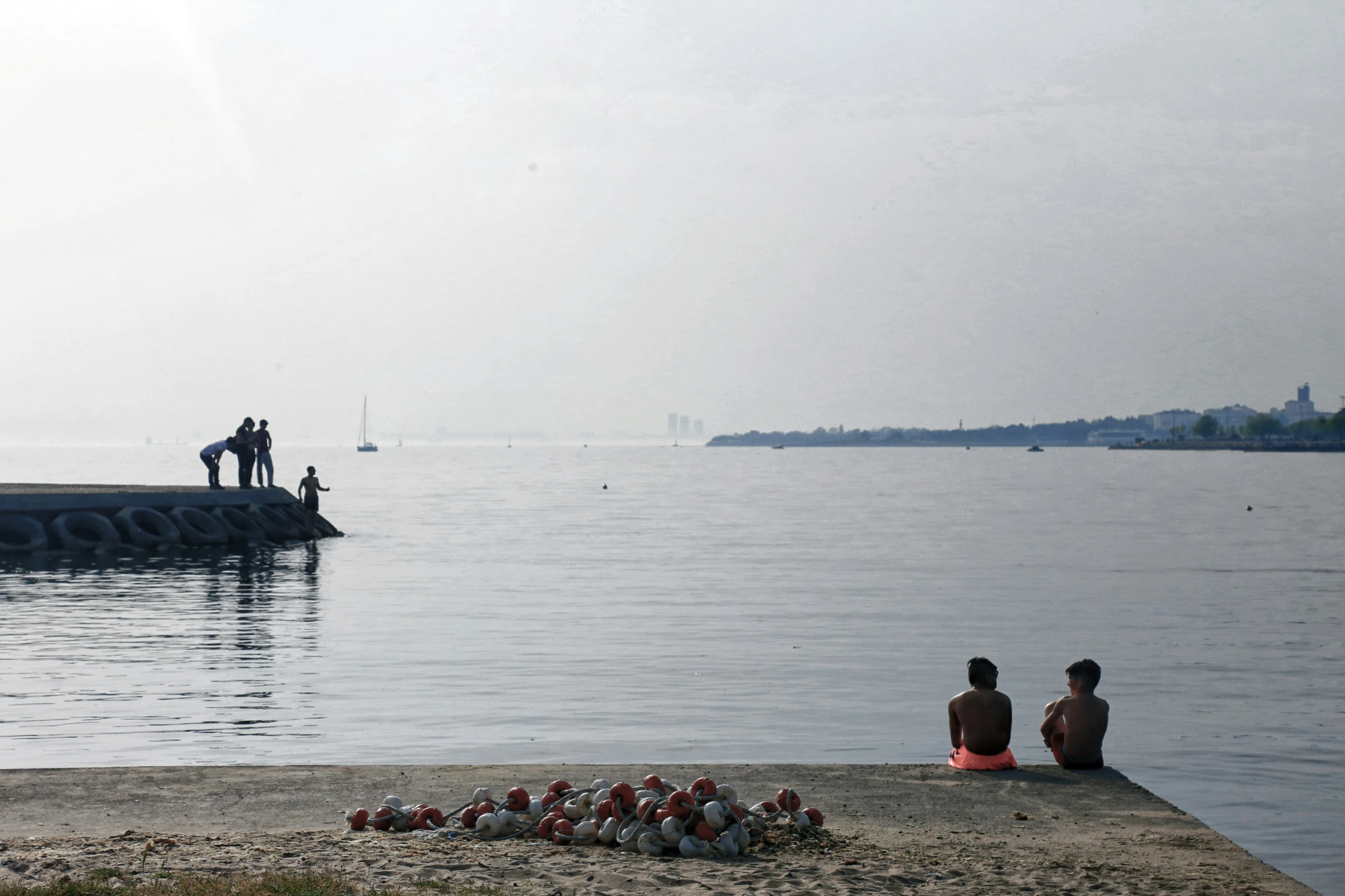 two people sit by the water as the seagulls fly