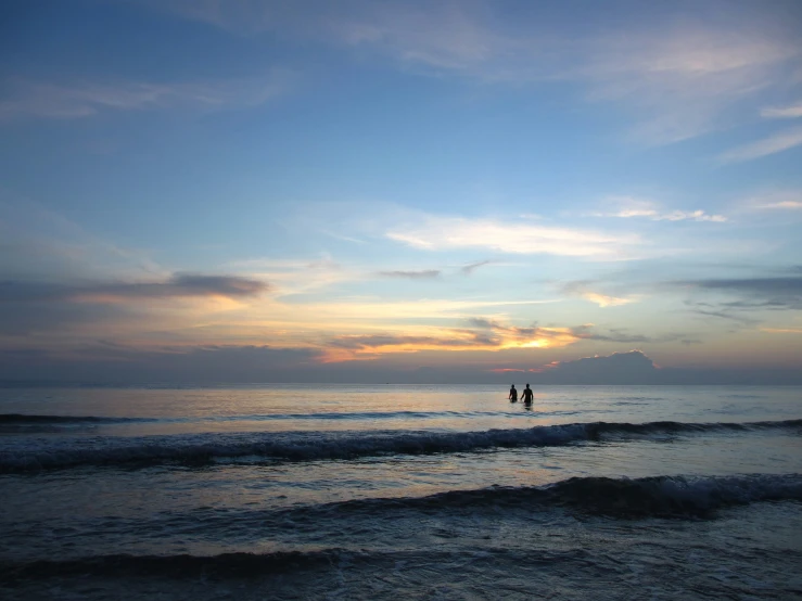 a couple holding hands while walking in the water at sunset