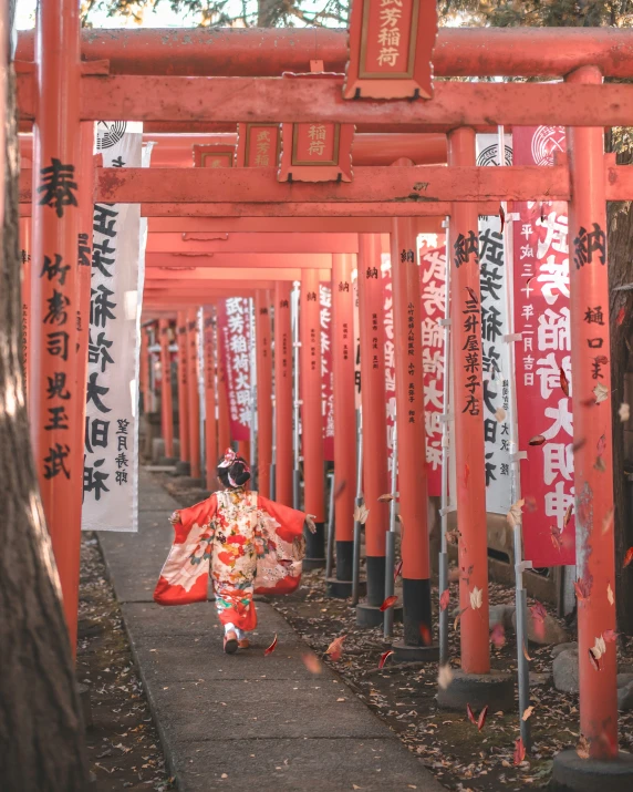 a girl wearing a kimono and red holding a parasol in front of some orange poles