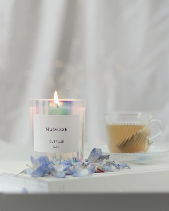 candle sitting in front of a glass cup with the word nudsense next to it