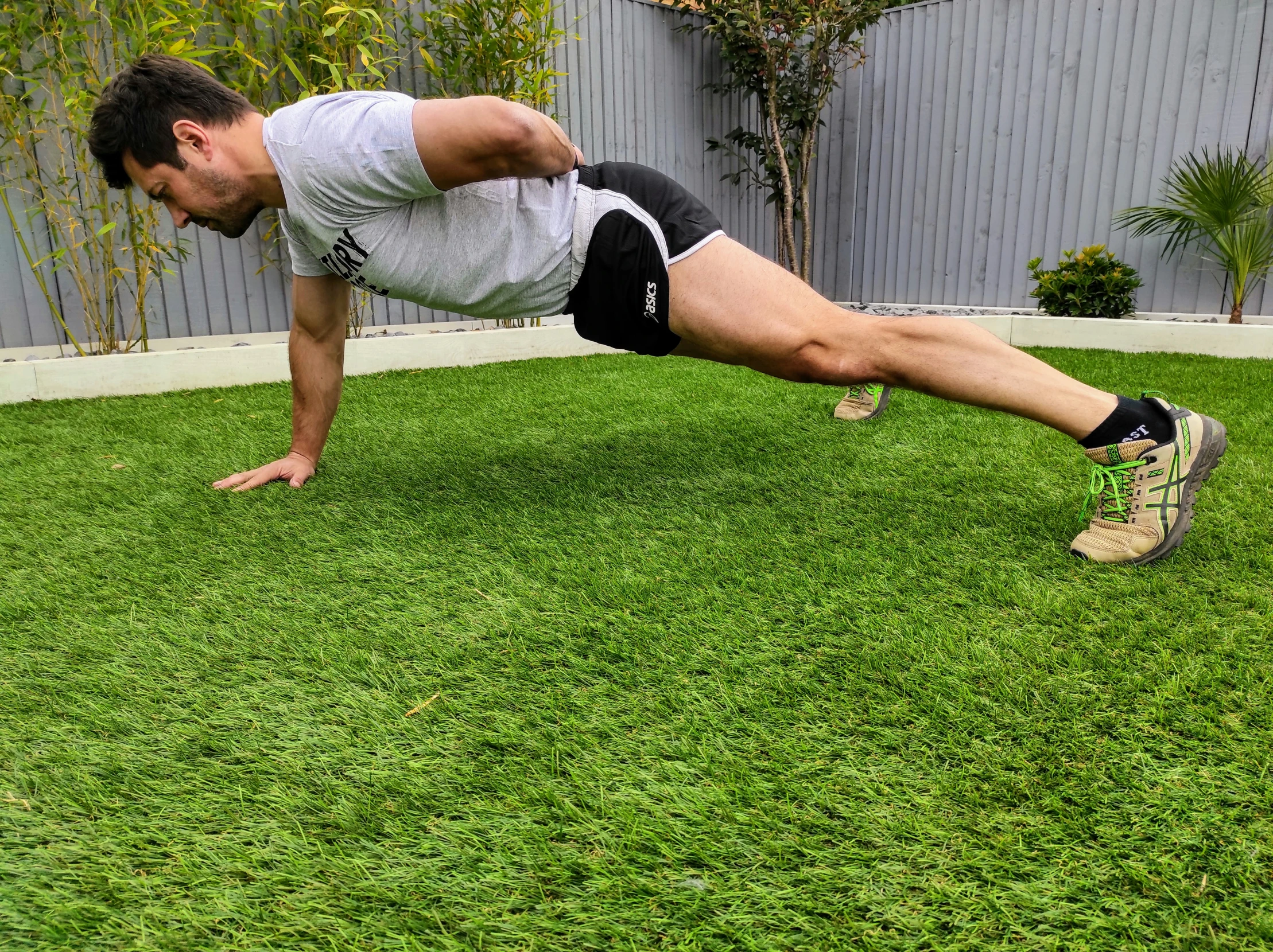 a man in white shirt and black shorts doing h ups on grass