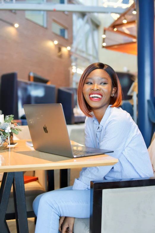 a woman sitting at a table smiling and using a laptop computer