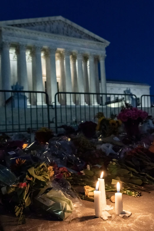 candles on the ground outside of a building with flowers