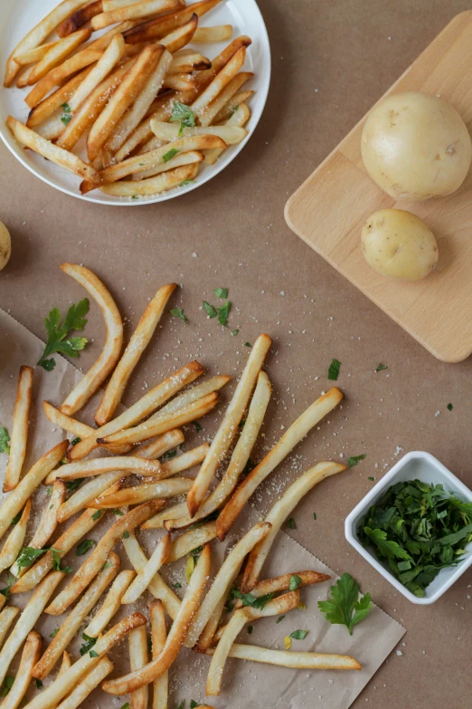 french fries are arranged on paper with garlic and parsley next to them