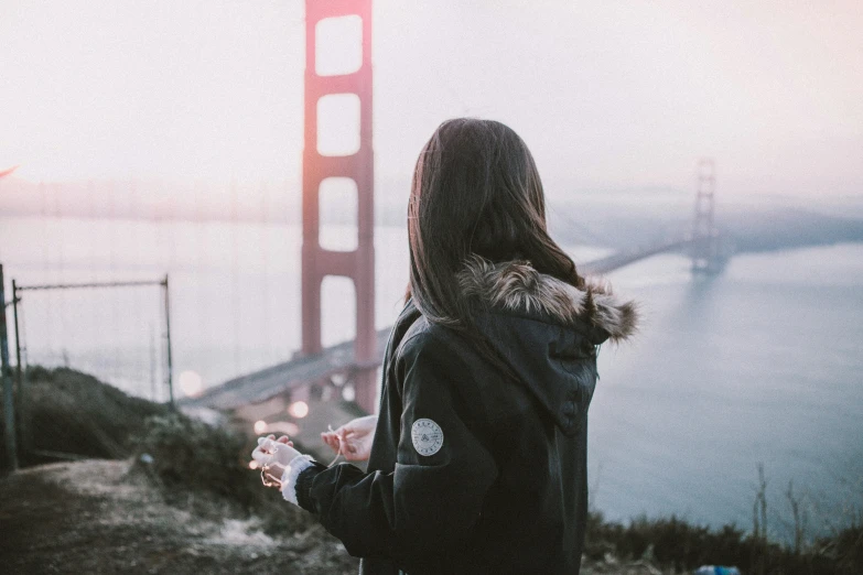 a girl is standing at the top of a hill next to a golden gate bridge