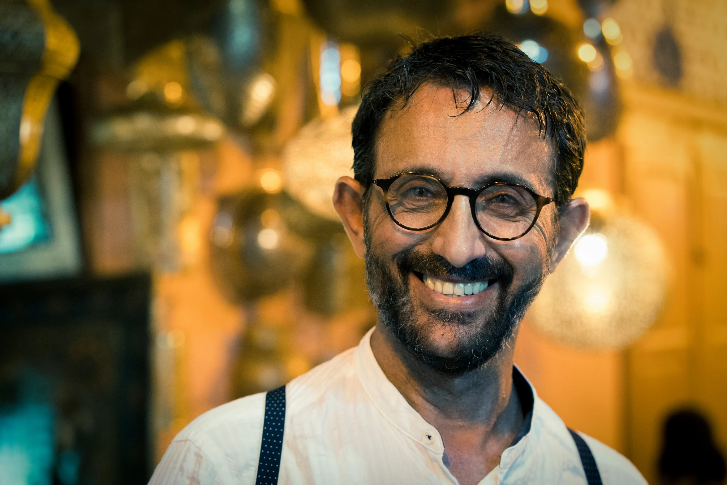 a man wearing suspenders and suspender suspenders standing in front of hanging glass pots