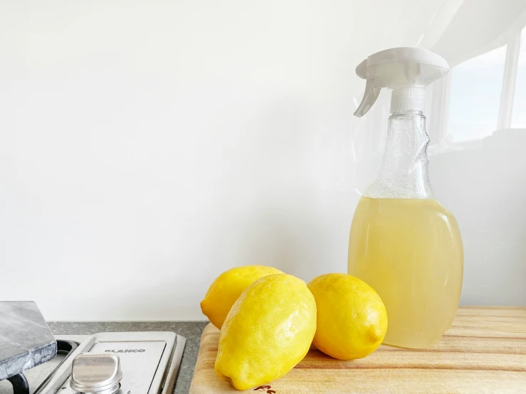 two lemons sit on a  board, beside a measuring spoon and bottle of lemon juice