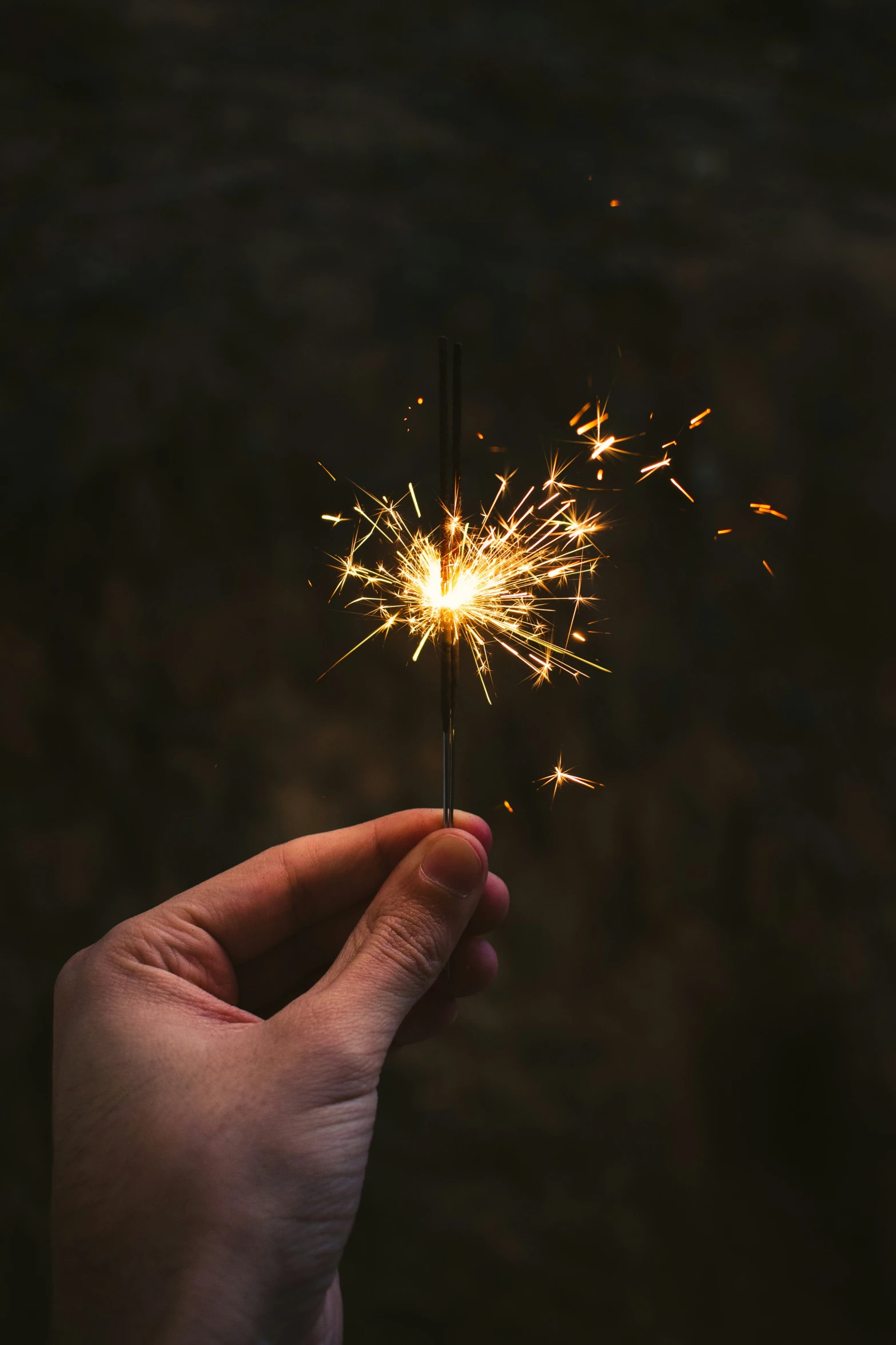 a hand holding sparkler in front of a dark background