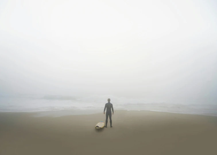 a man on a foggy beach with his surf board