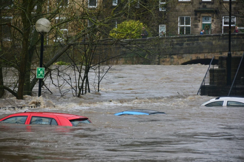 several cars are partially submerged as they approach a flooded street