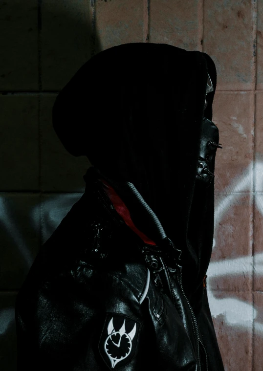 a person wearing a black hoodie next to a brick wall