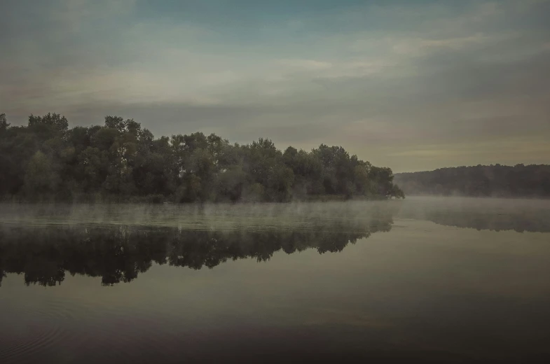 an empty lake is surrounded by fog and trees