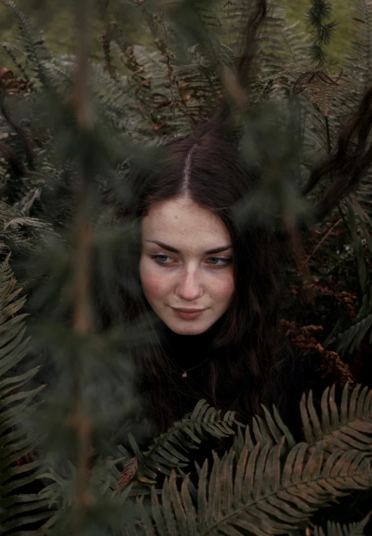 a young woman in a pine forest looking through leaves