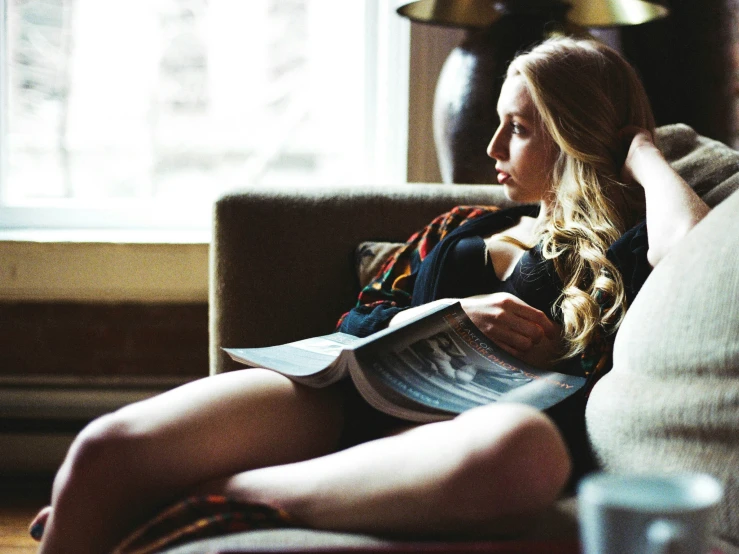 a woman is sitting in her couch reading a paper