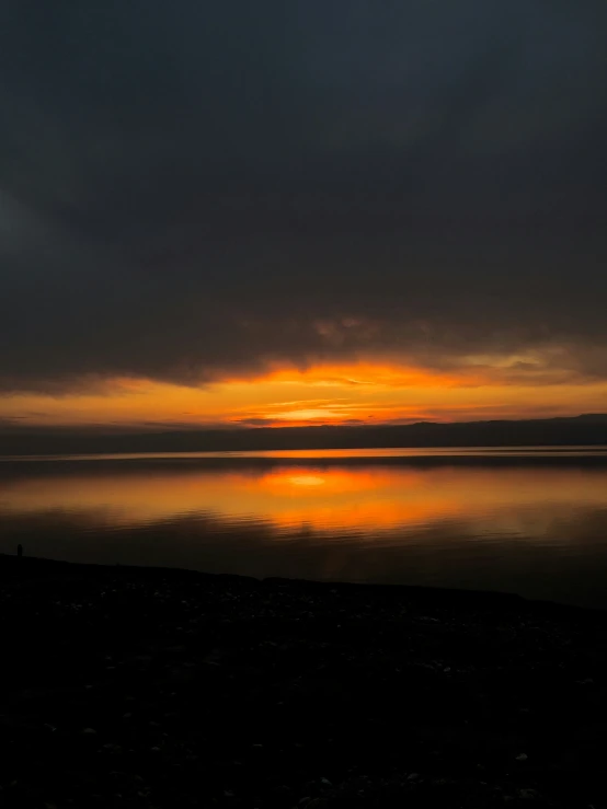 the sun sets over a large lake and mountains