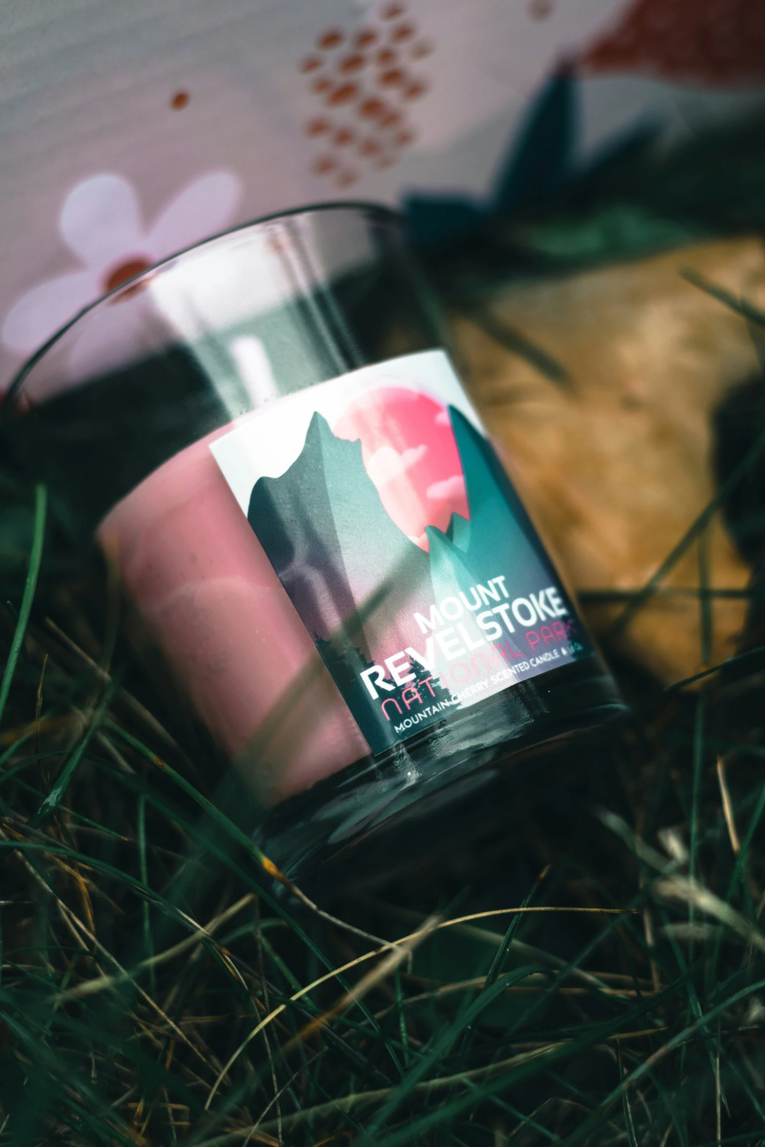 a pink candle sits in the grass with a cat