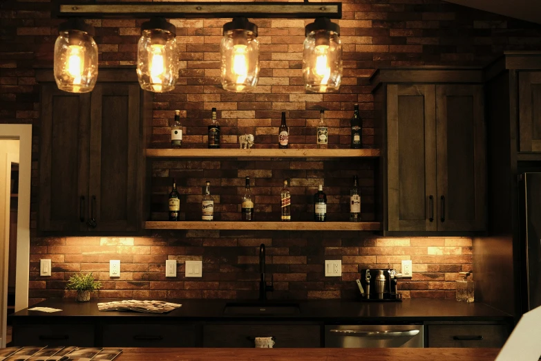 an organized dark kitchen has lit bottles and lights above