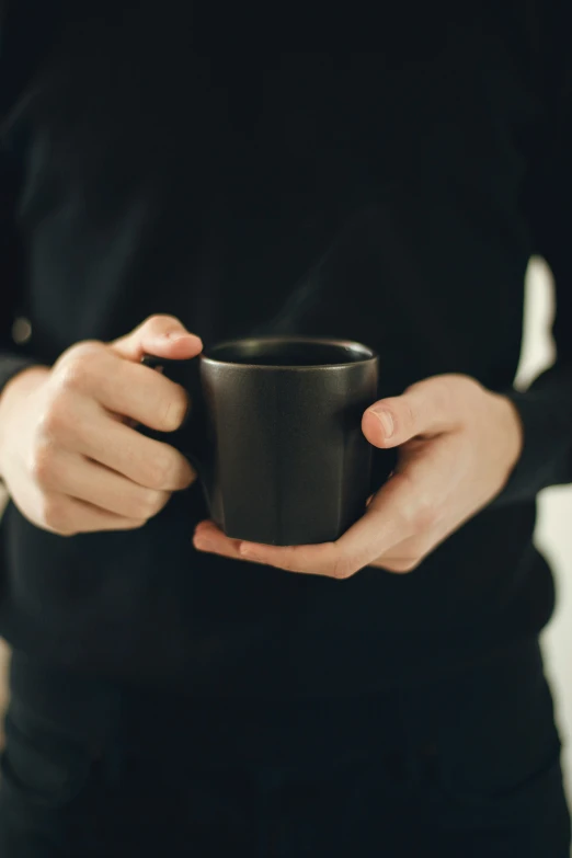 a person holds a black cup in their hands