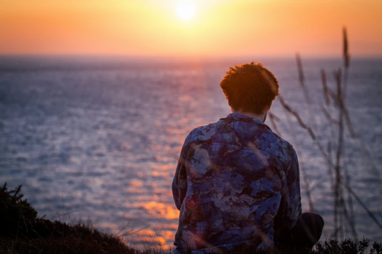 person sitting on a hill facing the ocean at sunset