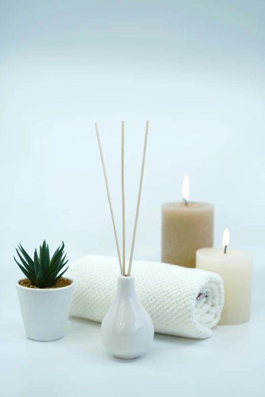 a white ceramic vase with sticks of reed sitting on a table next to candles