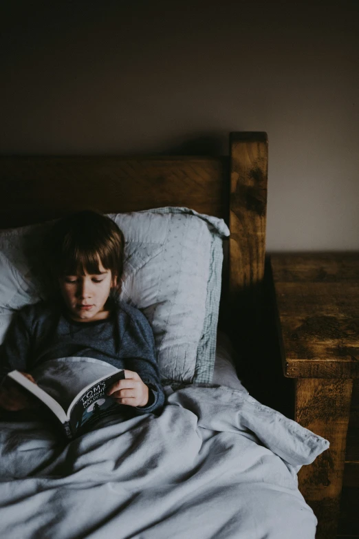 a little boy sitting in bed reading a book