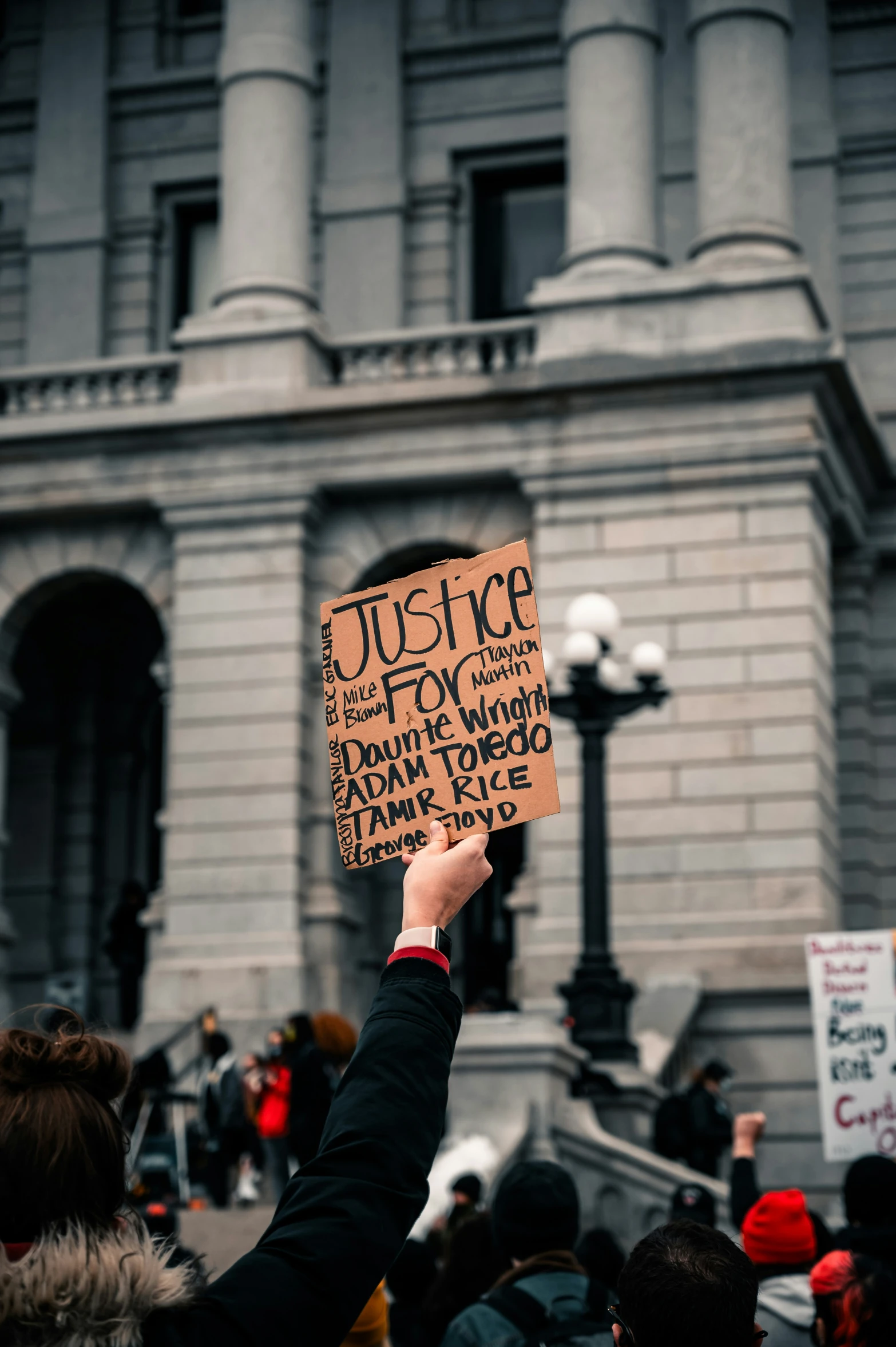 people in front of a building hold up signs that read justice for everyone