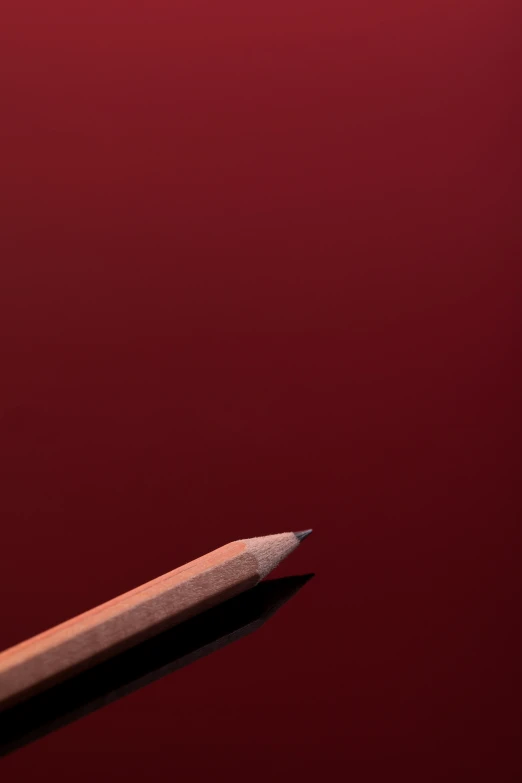 a single pencil is laying in front of a red wall