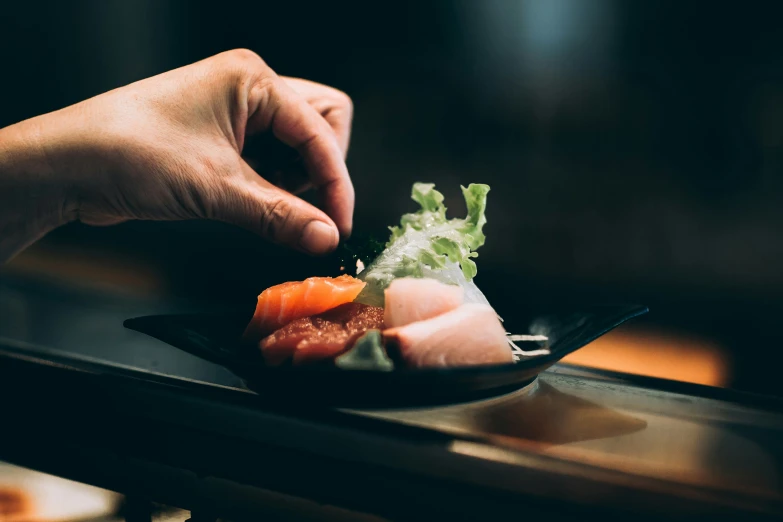 a person putting sushi on top of a black plate