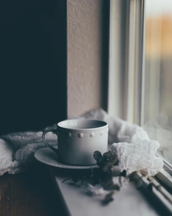 a cup with a saucer and napkins sitting on a window sill