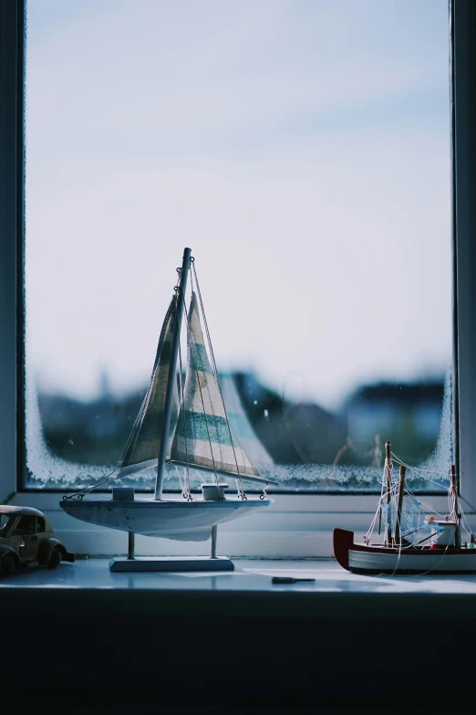 a model boat with sail in the foreground, sitting near a window